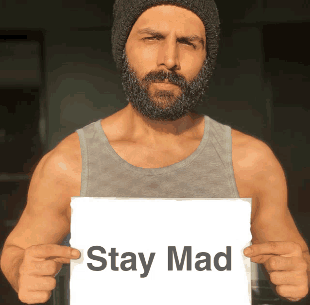 a man with a beard is holding a sign that says " stay mad "