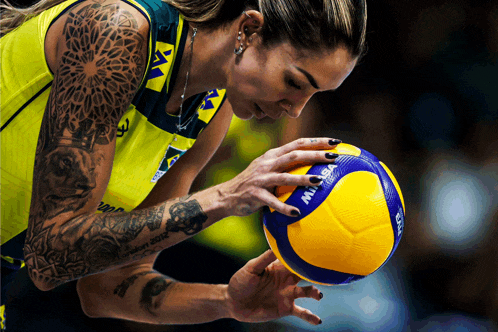 a woman with a tattoo on her arm holds a mikasa volleyball in her hand