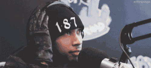 a man wearing a black hat with the number 187 on it is talking into a microphone .