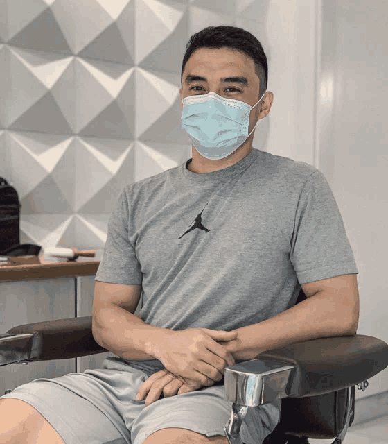 a man wearing a face mask sits in a chair with his hands folded