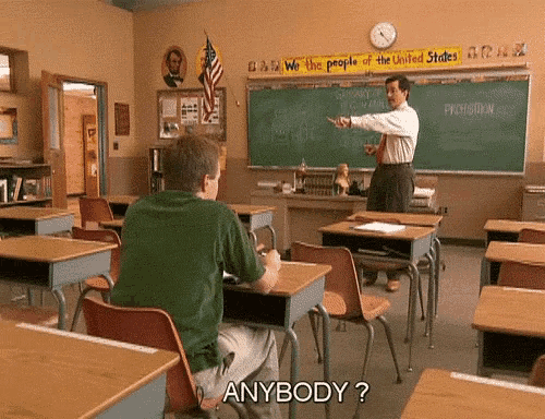 a man sitting at a desk in a classroom with a sign that says " we the people of the united states " on it