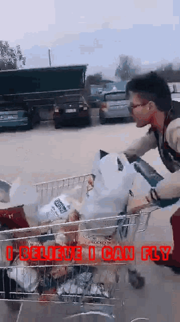 a man pushing a shopping cart full of groceries with the words " i believe i can fly " written on it