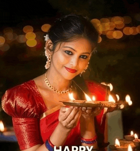 a woman in a red blouse is holding a tray of lit candles .