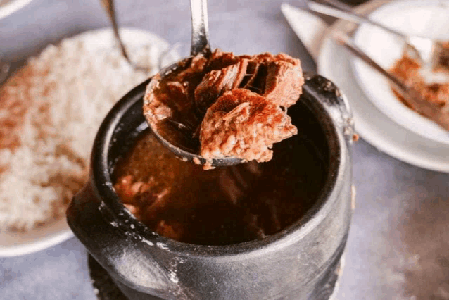 a ladle full of meat is being poured into a pot of stew