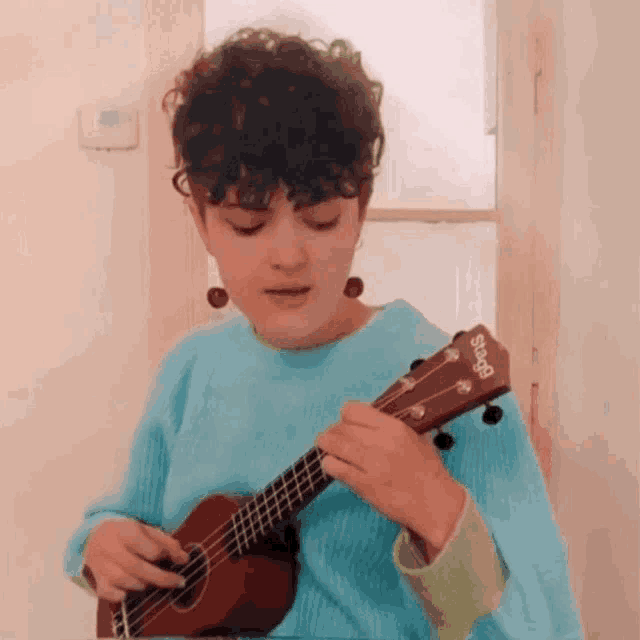 a woman in a blue sweater is playing a guitar with a sigg logo on it