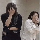 two women are standing next to each other in a bathroom covering their faces .