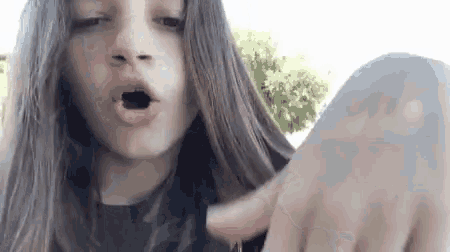 a young girl with long hair is making a funny face with her mouth open and her finger pointing .