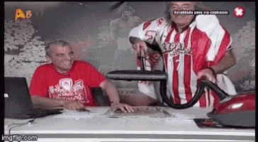 a man in a red and white striped shirt is holding a vacuum cleaner while sitting at a desk .