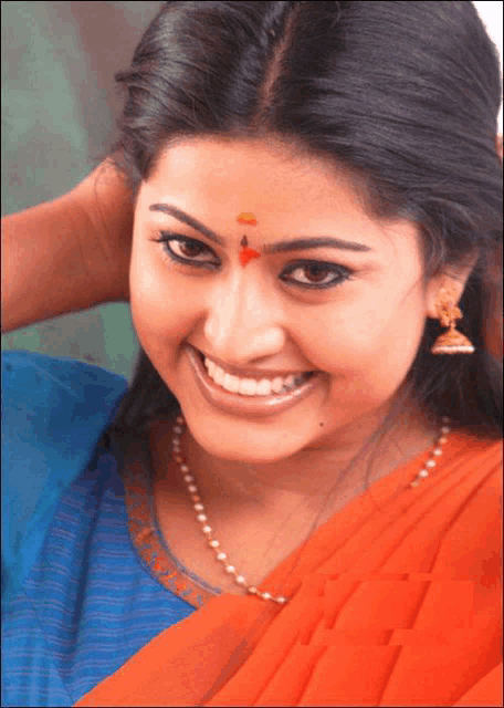 a woman wearing a blue shirt and an orange saree smiles for the camera