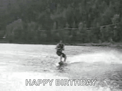 a black and white photo of a person water skiing on a lake with the words happy birthday written on the bottom .