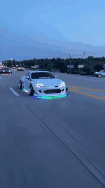 a white car is driving down a highway with a rainbow of lights on the tires .