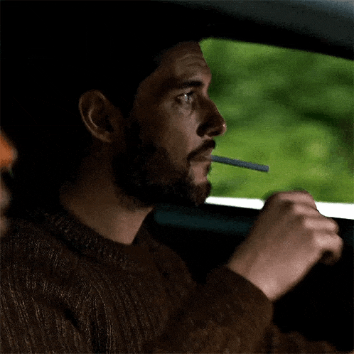 a man with a beard is smoking a cigarette while sitting in a car .