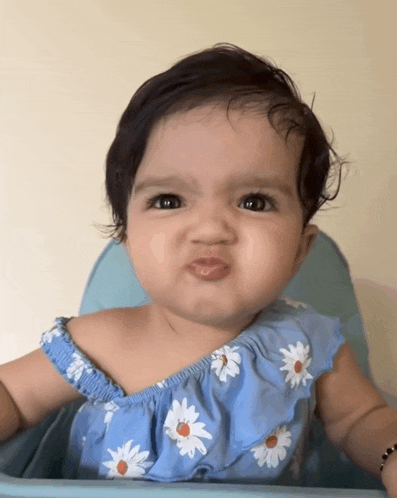 a baby girl wearing a blue dress with daisies on it making a funny face