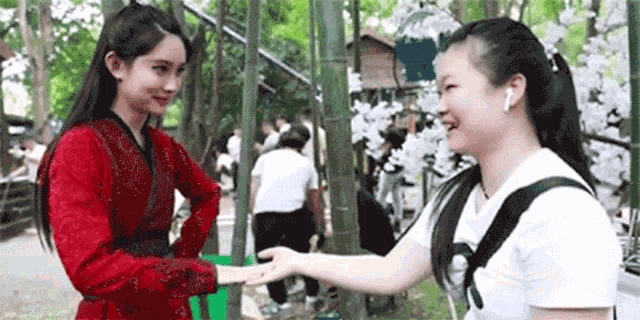 a woman in a red dress is shaking hands with another woman in a white shirt in a park .