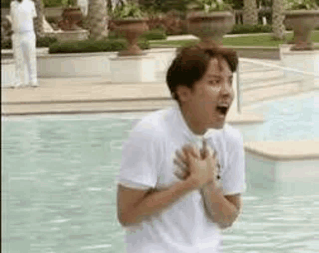 a man in a white shirt is standing next to a swimming pool with his hands on his chest .