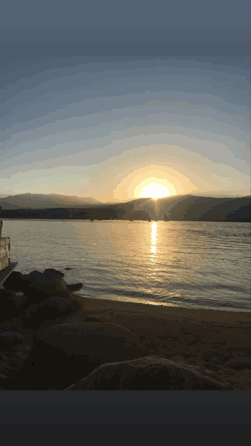 the sun is setting over a lake with mountains in the background