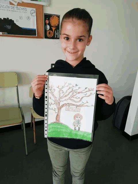 a young girl holds up a drawing of a tree with a sign that says " edición de prompta " on it