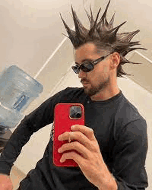 a man wearing sunglasses and a mohawk is taking a selfie with his phone .