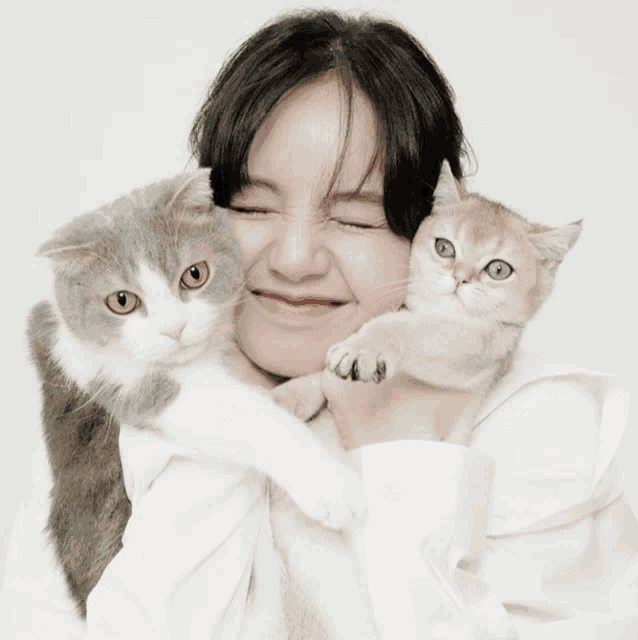 a woman in a white shirt holds two cats in her arms