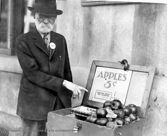 a black and white photo of a man standing next to a box of apples