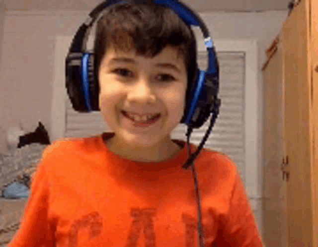 a young boy wearing headphones and a red shirt with the letter t on it smiles for the camera