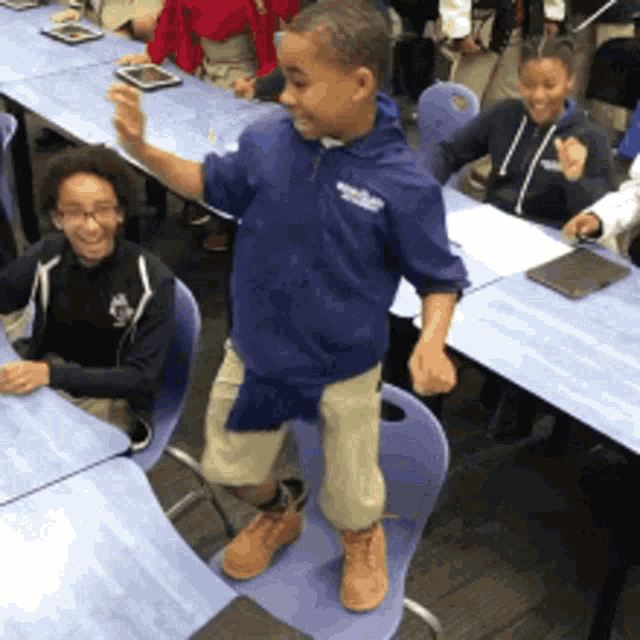 a boy wearing a blue shirt that says ' brooklyn ' on it stands in front of a classroom full of children