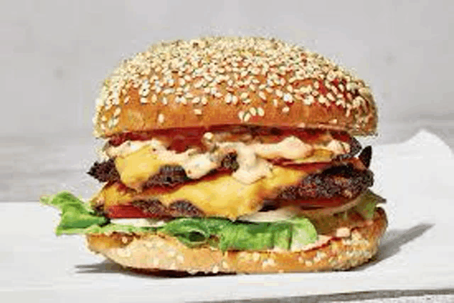 a close up of a hamburger with lettuce , tomatoes , and cheese on a sesame seed bun on a table .