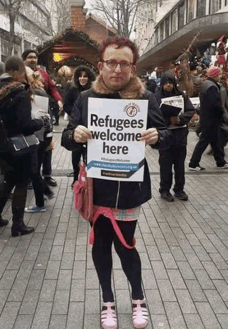 a man holds a sign that says refugees welcome here