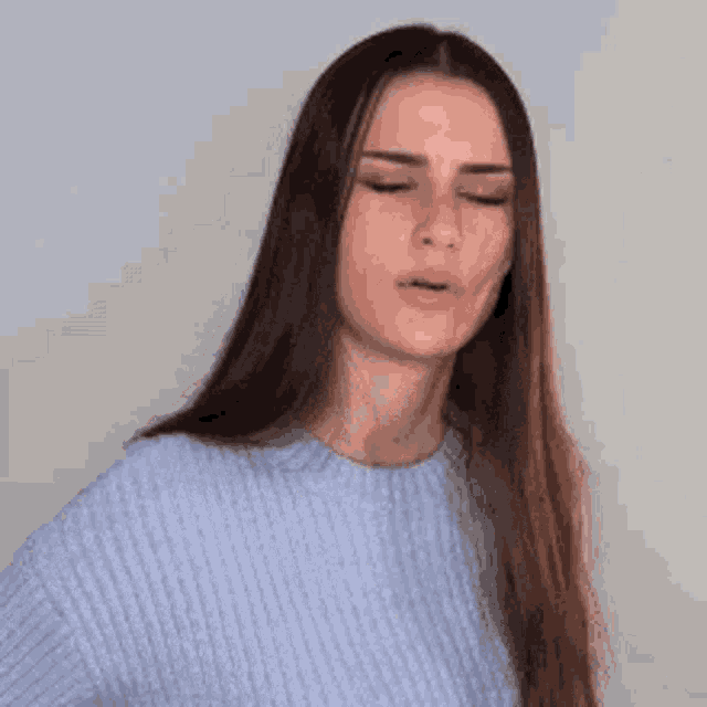 a woman with long hair and a blue sweater is making a funny face .