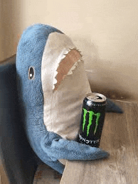 a stuffed shark is sitting next to a can of monster energy drink on a table .