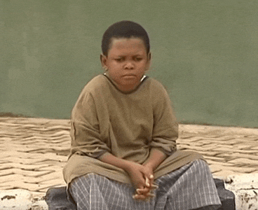 a young boy is sitting on the ground with his hands folded and looking at the camera .