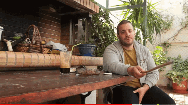 a man sits at a table with a cigarette in his hand and a cup of coffee in front of him