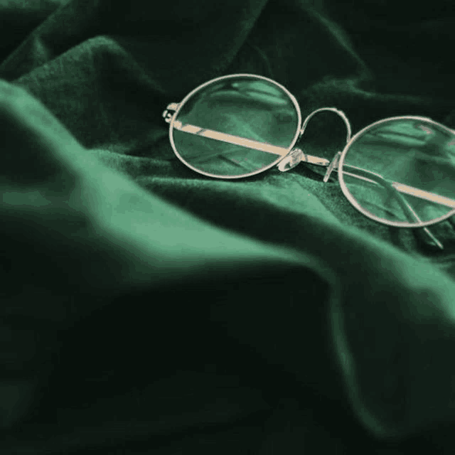 a pair of round glasses is laying on a green cloth .