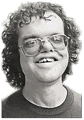 a man with curly hair and glasses is smiling for the camera .