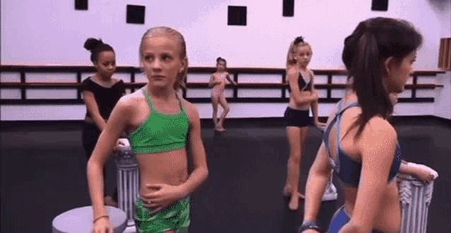 a group of young girls are standing in a dance studio wearing bikinis .