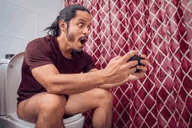 a man is sitting on a toilet playing a video game while holding a controller .