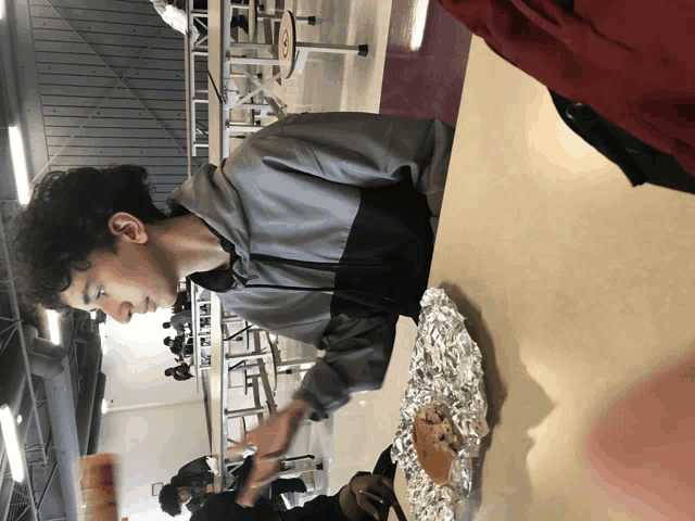 a young man sits at a table in a cafeteria with a piece of aluminum foil on it