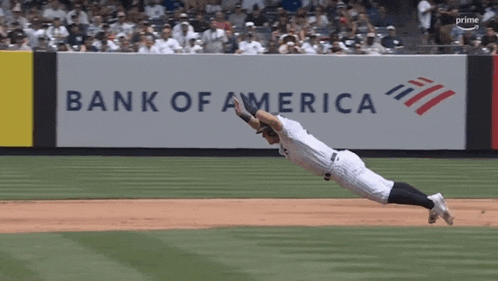 a baseball player dives to catch a ball in front of a bank of america banner