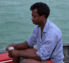 a man in a blue shirt is sitting on a boat with a can of soda in his hand .