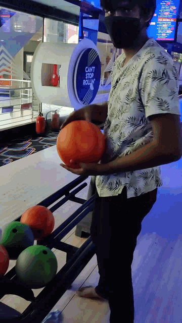 a man wearing a mask holds a bowling ball in front of a sign that says " can 't stop rolling "