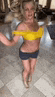 a woman in a yellow bikini top and blue shorts is dancing in a room .