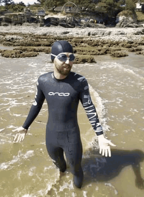 a man in a wetsuit is standing in the water on a beach .