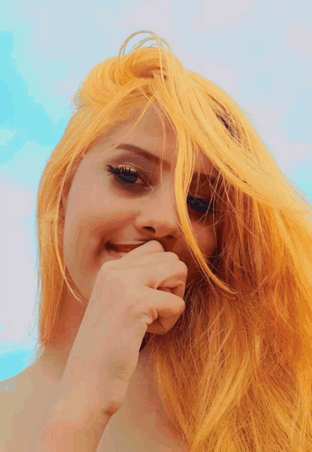 a woman with bright yellow hair is smiling and covering her mouth with her hand