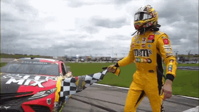 a race car driver is waving a checkered flag in front of a race car sponsored by m & m 's .