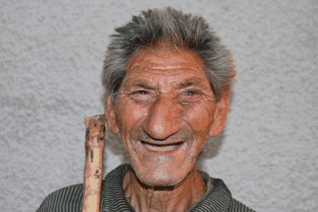 an elderly man with a cane in his right hand smiles for the camera