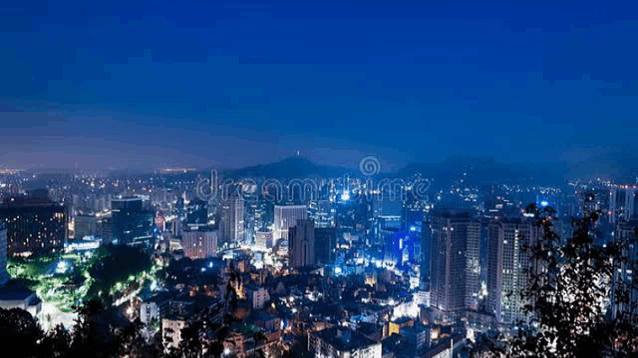 an aerial view of a city at night with lots of buildings and mountains in the background .