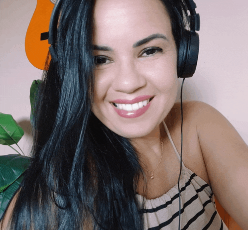 a woman wearing headphones smiles in front of an orange guitar