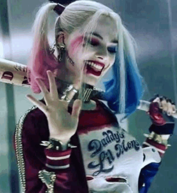 harley quinn from suicide squad is wearing a daddy 's lil monster shirt and holding a bat .