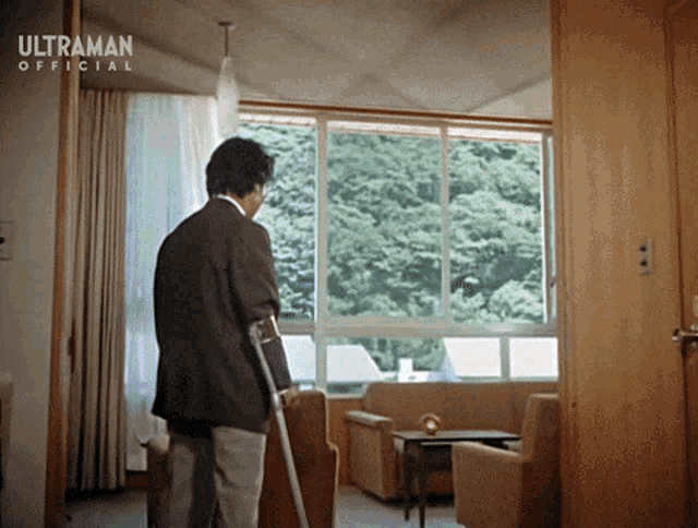 a man with crutches is standing in a living room with ultraman official written on the ceiling