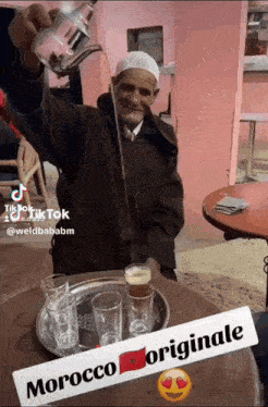 a man is pouring a drink from a teapot on a table with a sign that says morocco originale on it